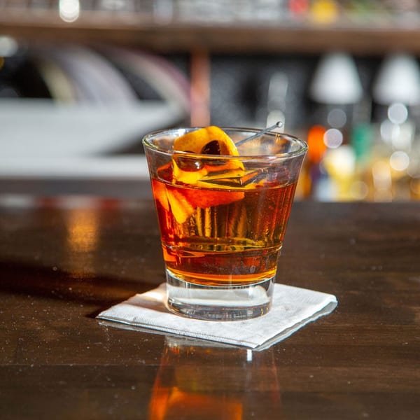 A Red Barn Restaurant cocktail, amber-colored with orange peel and cherry, on a bar.