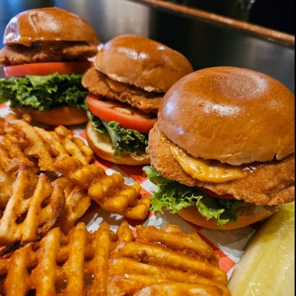 Three crispy chicken sliders with lettuce, tomato, and waffle fries from The Red Barn.