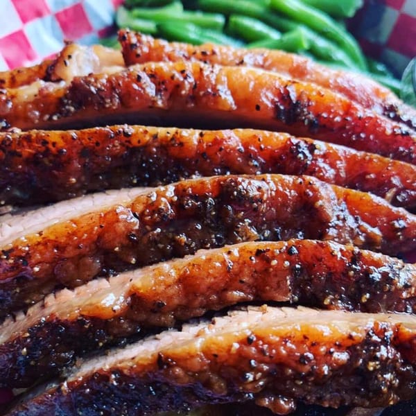 Close-up of sliced brisket with a dark, peppery crust, served with green beans.