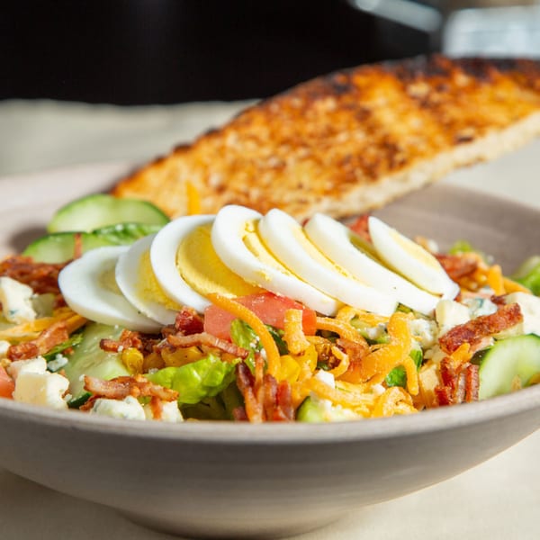 A close-up of a Cobb salad with sliced eggs, bacon, cheese, and cucumber, served with toast.