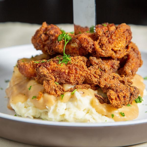 Crispy fried chicken tenders piled high on a bed of mashed potatoes with gravy, garnished with parsley.