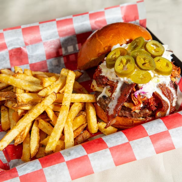 A Red Barn Restaurant burger with bacon, jalapenos, and fries in a red checkered basket.